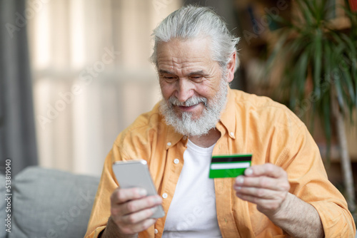 Happy senior man using smartphone and credit card at home