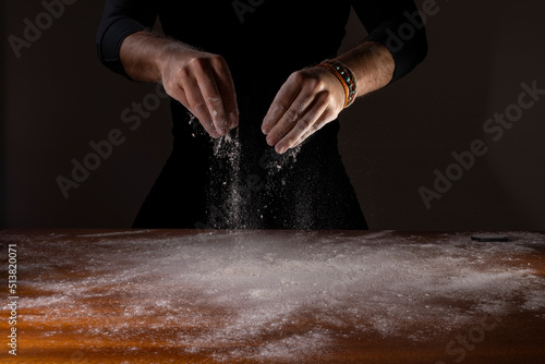 Mão derrubando farinha branca de trigo sobre a mesa com fundo preto photo