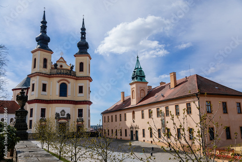 Litomysl, Czech Republic, 17 April 2022: Church of the Finding of the Holy Cross and Piarist dormitory near castle, Regional Museum baroque building with tower at sunny summer day, stone statues
