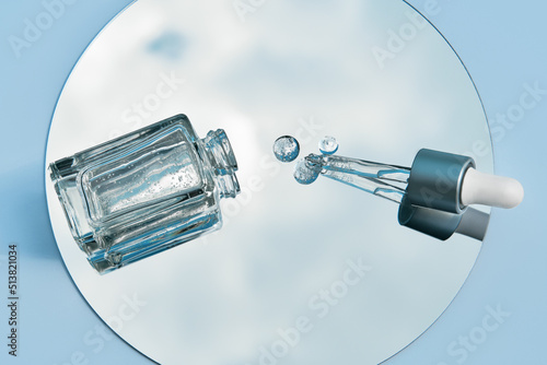 Flat lay of pipette with serum and cosmetic bottle on the mirror reflected in the blue sky. Organic cosmetics. Top view flat lay, copy space. Cosmetics, SPA branding, mock-up.