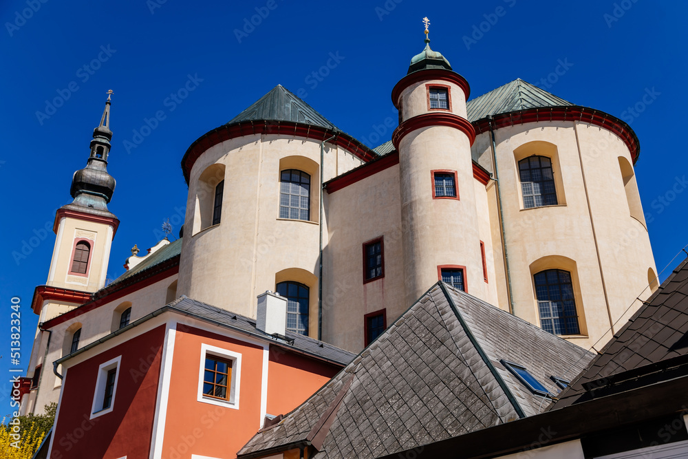 Litomysl, Czech Republic, 17 April 2022: Church of the Finding of the Holy Cross and Piarist dormitory near castle, baroque building with tower at sunny summer day, stone statues in the garden