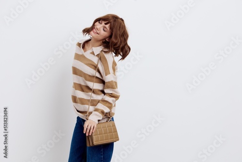  cheerful woman stands on a white background in a stylish striped sweater with a beige bag on her shoulder and smiles cheerfully while standing in a relaxed pose pressing the bag to her body