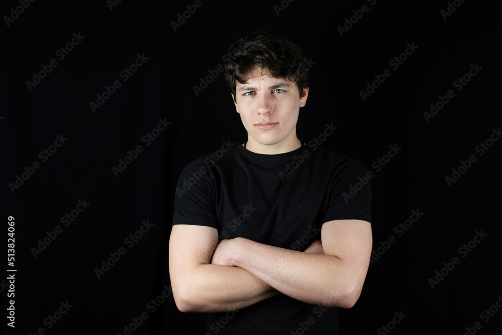 The young man is still a teenager with a confident look, folded his arms in front of him and looks with confidence in the future. Cute guy with dark hair on a dark background The young man is still a teenager with a confident look, folded his arms in front of him and looks with confidence in the future. Cute guy with dark hair on a dark background