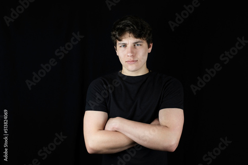 The young man is still a teenager with a confident look, folded his arms in front of him and looks with confidence in the future. Cute guy with dark hair on a dark background © Мар'ян Філь