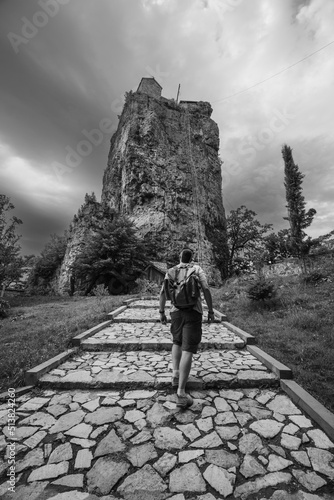 Male tourist with a backpack, walking, posing. Katskhi pillar. Man's monastery. Black and white. The orthodox church rocky cliff. Georgia. Travel and vacation. Vertical photo. Back view