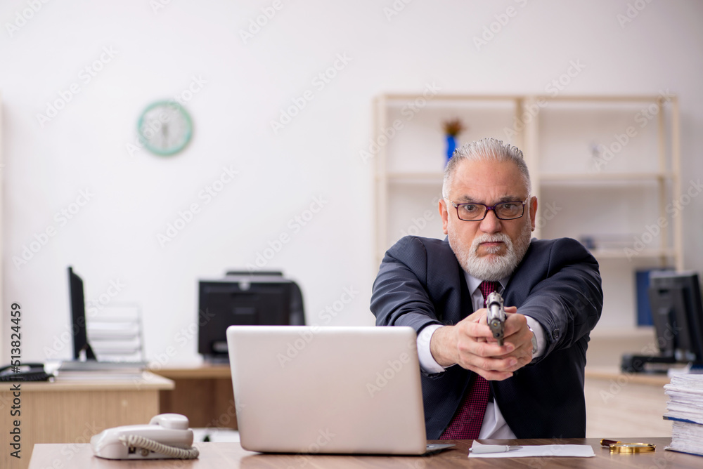 Old businessman holding gun at workplace Old businessman holding gun at workplace