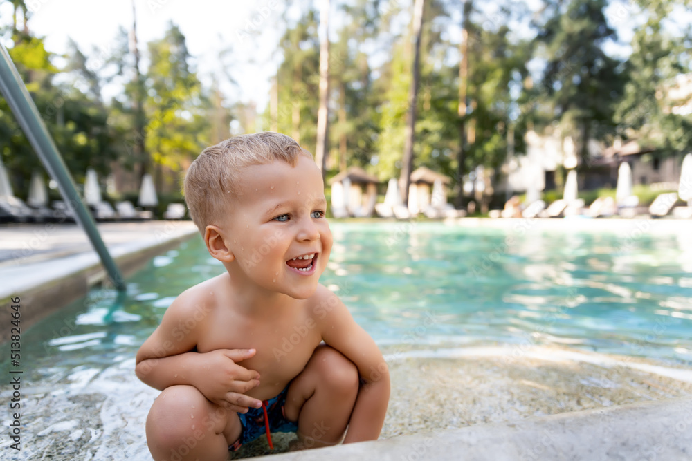 Little cute adorable blond playful beautiful caucasian active toodler boy enjoy playing at pool edge at summertime outdoor sea forest resort area. Happy kid friend leisure vacation travel concept