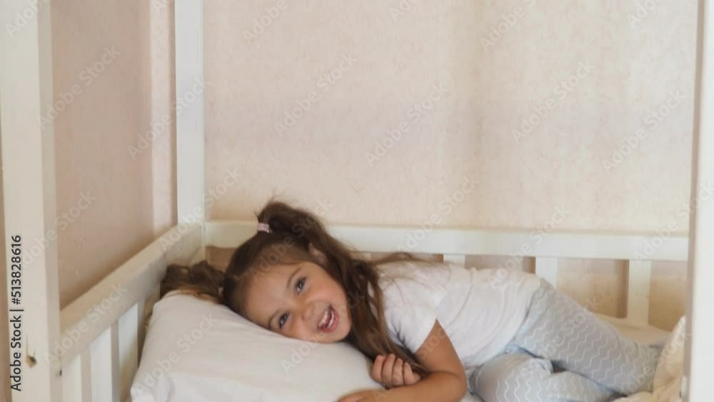 little girl at home in bed in pajamas, with long hair, ponytails. doesn't want to sleep, plays around. time before bed. good night. kicks the blanket. family before bed little girl at home in bed in pajamas, with long hair, ponytails. doesn't want to sleep, plays around. time before bed. good night. kicks the blanket. family before bed
