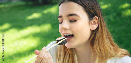 A young woman eating sushi in nature, maki roll close-up.