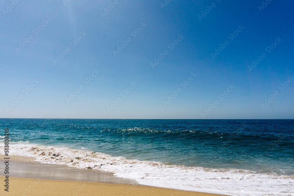 Ocean seascape with waves washing up onto sandy beach under a clear blue sky 