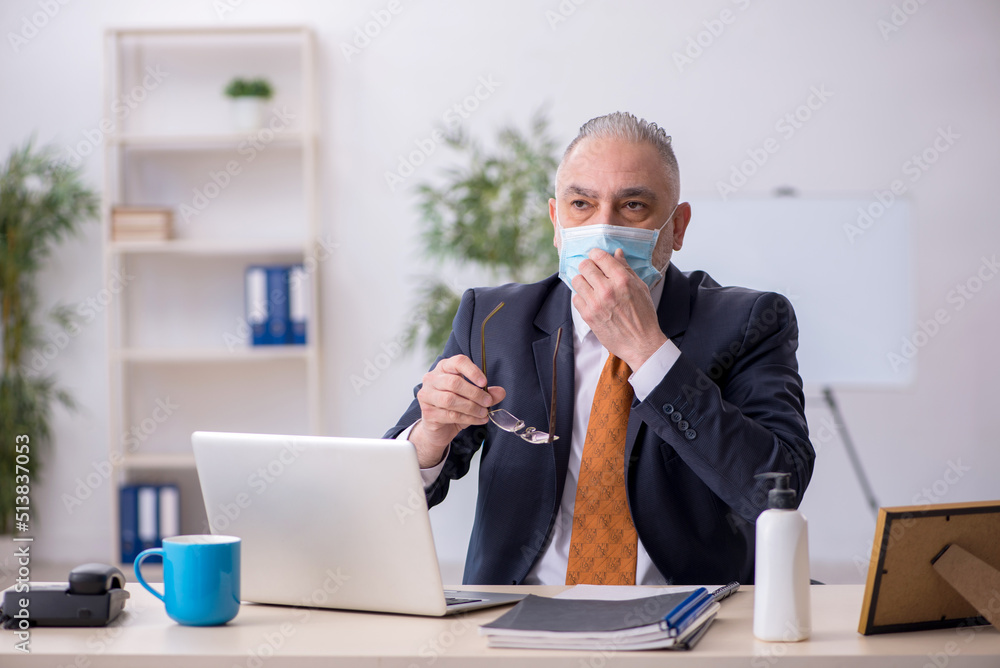 Old male employee working in the office during pandemic