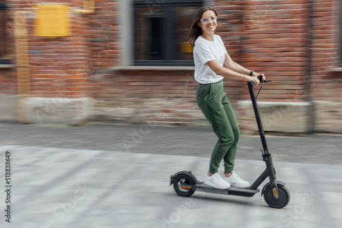 Woman in white t shirt and sneakers rides an electric scooter