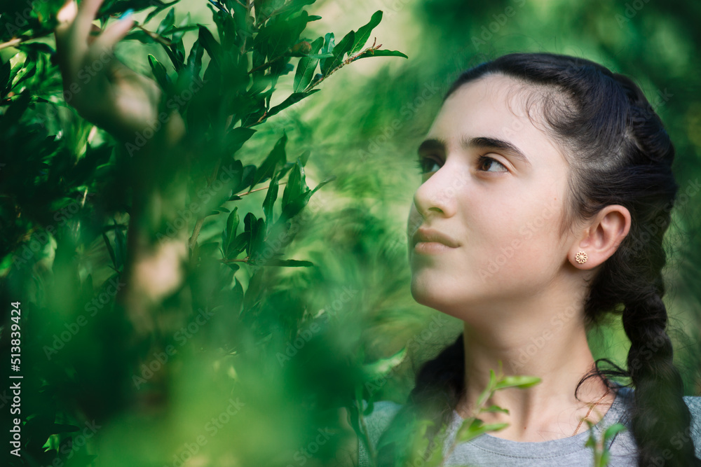 Closeup of nice girl with green bokeh in garden holding pomegranate tree branch in summer
