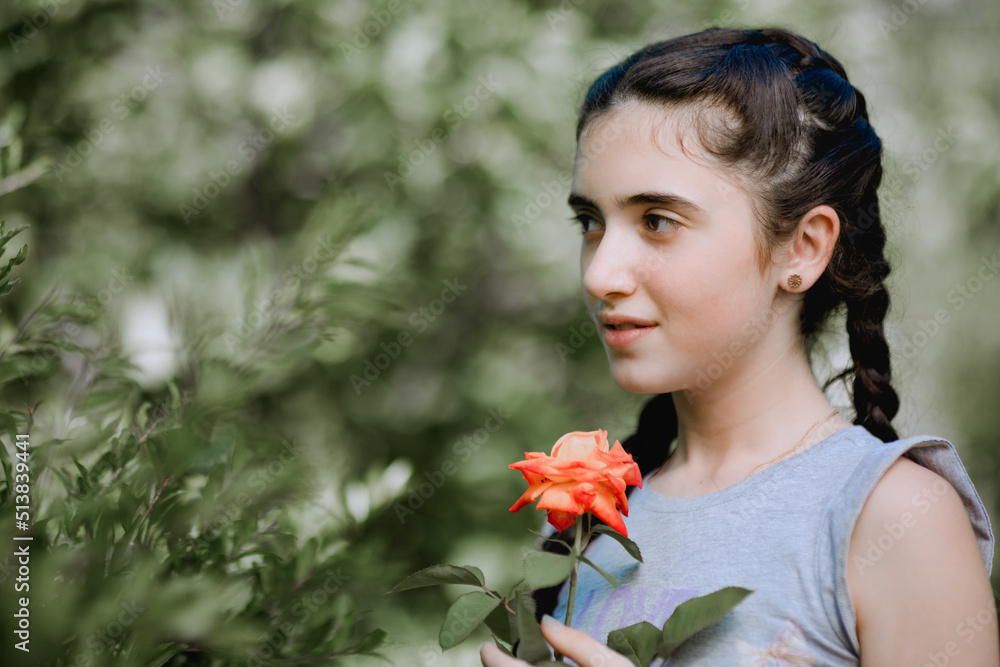 Desatuarted portrait of little armenian girl standing next to the tree in garden and holding the rose