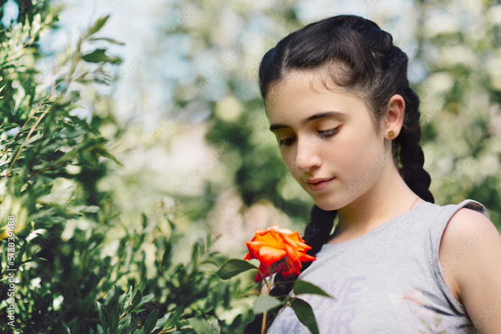 Nice emotion of cute little girl holding and looking down at rose in garden