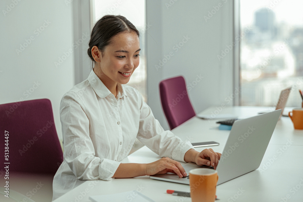 Smiling asian business woman working laptop sitting in modern office. High quality photo Smiling asian business woman working laptop sitting in modern office. High quality photo