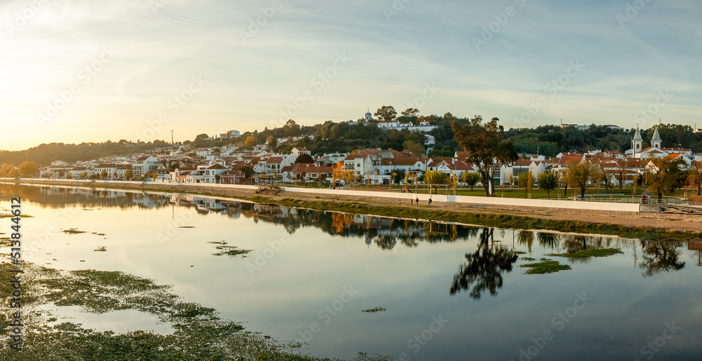 Panoramic view of the village of Coruche in Portugal at sunset, with the river Sorraia in the foreground and the riverside houses reflected in the waters.