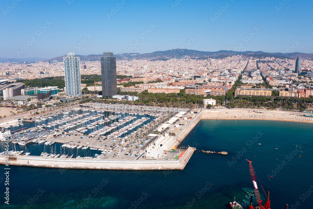 Scenic aerial view of famous Olympic Harbor Marina with docked white pleasure yachts on background of modern cityscape of Barcelona on Mediterranean coast on summer day, Spain..