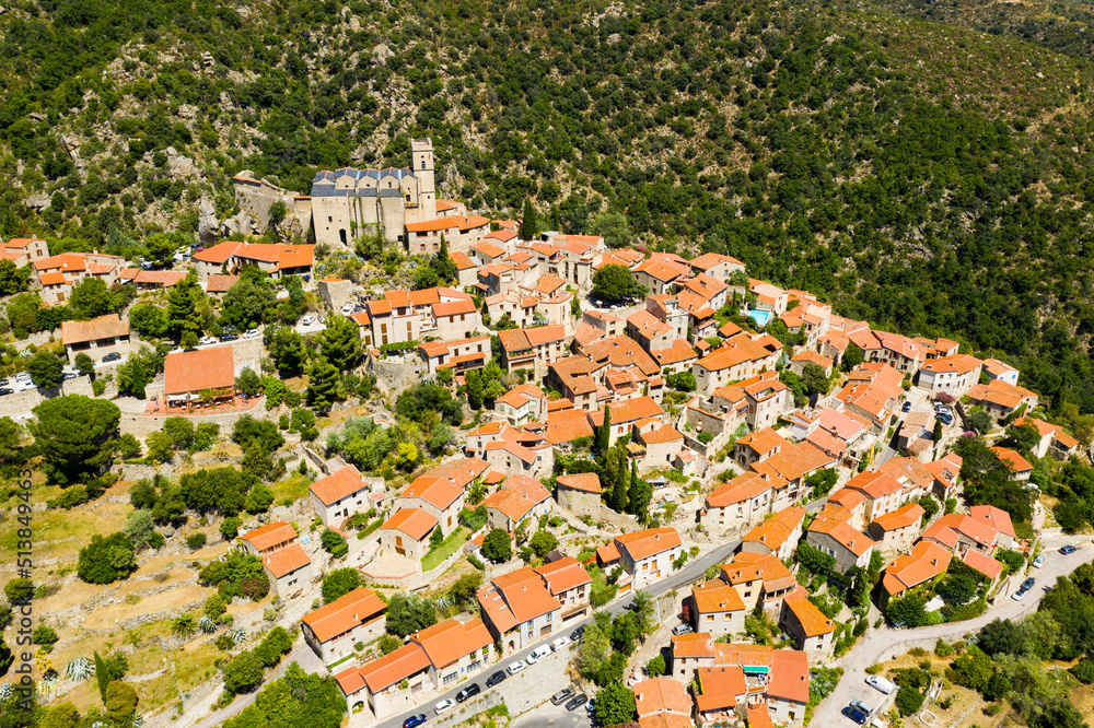 General summer view of picturesque French village of Eus in natural region of Conflent with tightly grouped houses, medieval church and castle ruins on top of hill