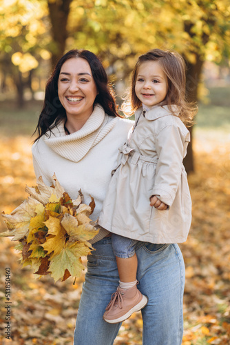 Happy mother holding little daughter in her arms in autumn park