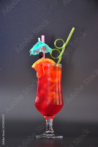 Sex on the beach, a refreshing cocktail in a tall glass with an umbrella and straws on a black background.