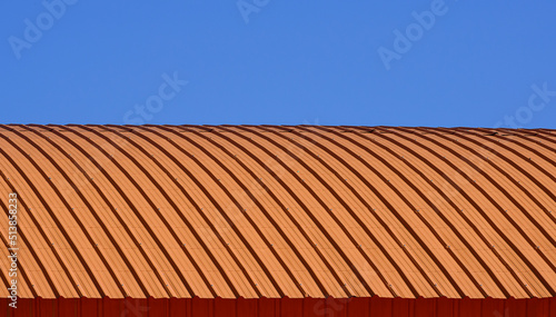 Curve line pattern of orange corrugated steel curved roof against blue clear sky background