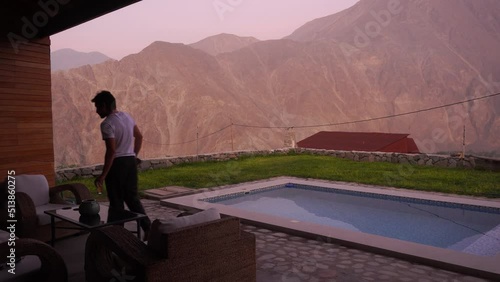 a man with a shirt that says “I love you Peru” having a drink sitting on the terrace with a swimming pool in a country house with a beautiful view of mountains in the highlands of Lunahuana at sunset photo