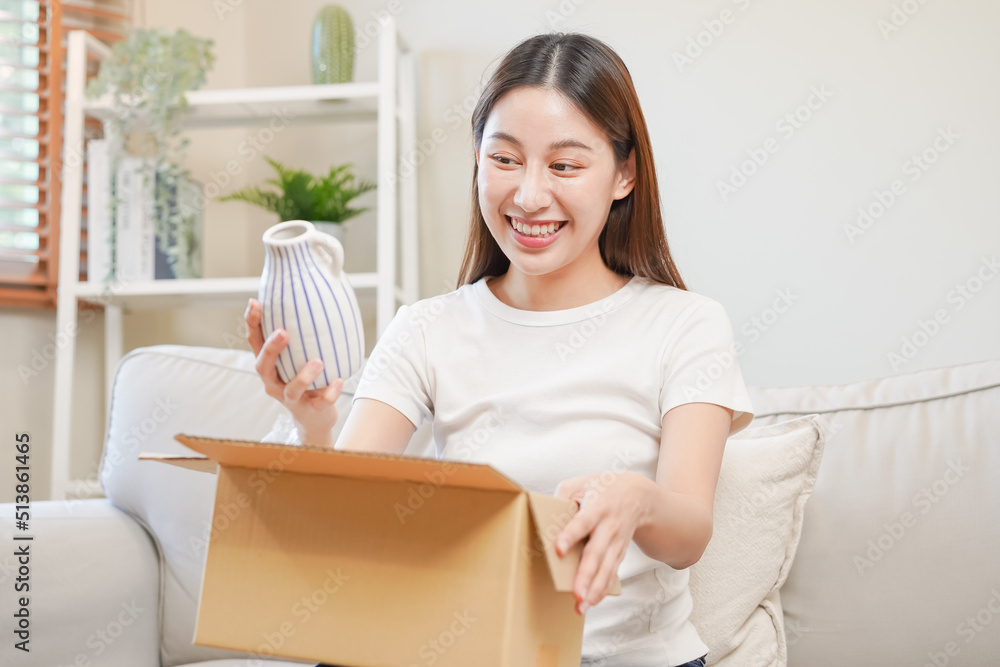 Happy excited, asian young woman, girl customer sitting on sofa at home, opening and unpacking cardboard box carton parcel after buying ordering present, shopping online, delivery service concept. Happy excited, asian young woman, girl customer sitting on sofa at home, opening and unpacking cardboard box carton parcel after buying ordering present, shopping online, delivery service concept.