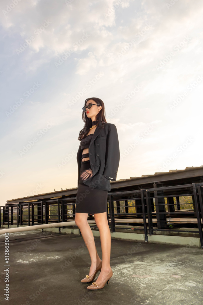 Fashionable concept, Fashion woman wear black dress with sunglasses to pose on rooftop with sunset
