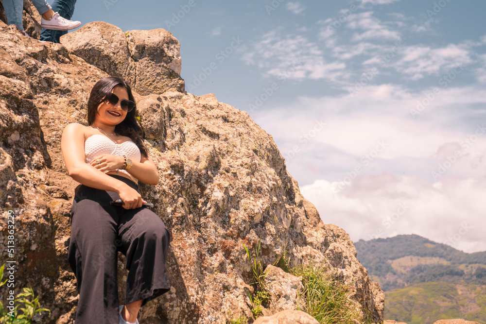 Naklejka premium Beautiful teenage girl in sunglasses lying on a rock on top of a mountain looking at camera and smiling in Jinotega Nicaragua