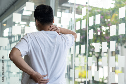 back view of a young man holding his neck and back in pain Lower back pain. Touching the neck and back because it hurts. © ArLawKa