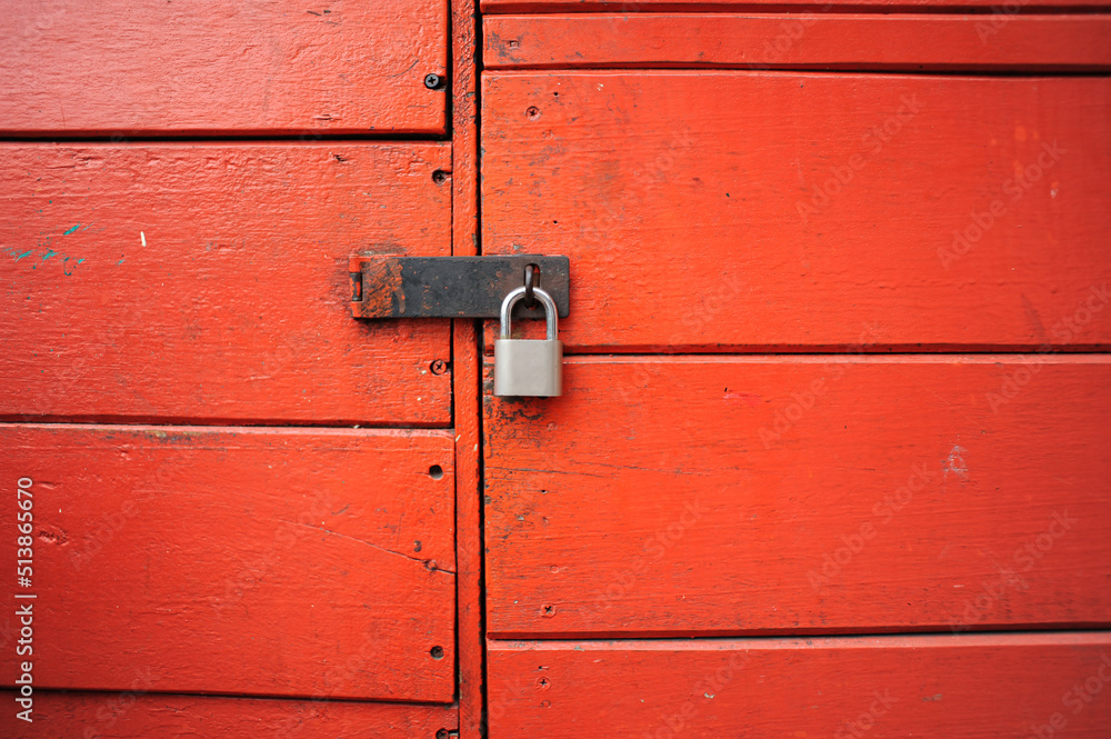 Close-up of an old red wooden door with a gray metal padlock. Close-up of an old red wooden door with a gray metal padlock.