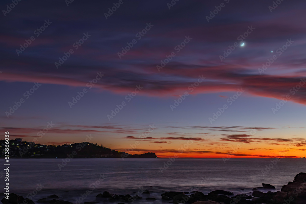 First light over the ocean with 9 percent sliver of moon and stars