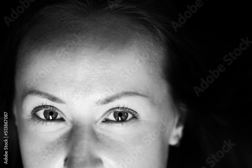 Black and white photograph of an attractive woman. A large portrait on a dark background. Macro photo, top of the face. Front view.
