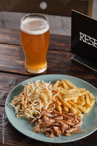 Appetizer for beer. Assorted smoked meat, salted cheese and French fries in a plate on a wooden table. Vertical orientation, copy space, no people