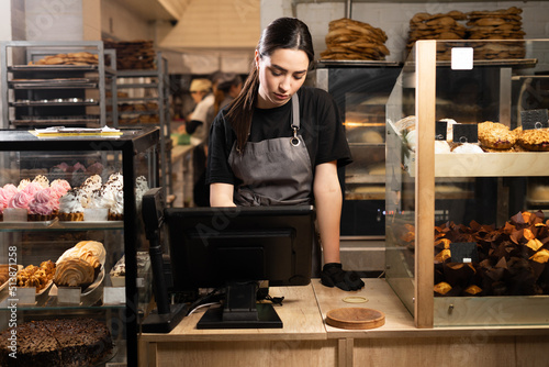 pretty female baker working in bakery shop standing near the showcase of copyspace. Satisfied baker with breads in background. Small business