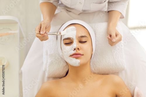 Top view of cosmetologist make moisturizing nourishing face mask to woman client in beauty salon. Beautician or dermatologist do facial procedures to patient in clinic. Cosmetology concept.