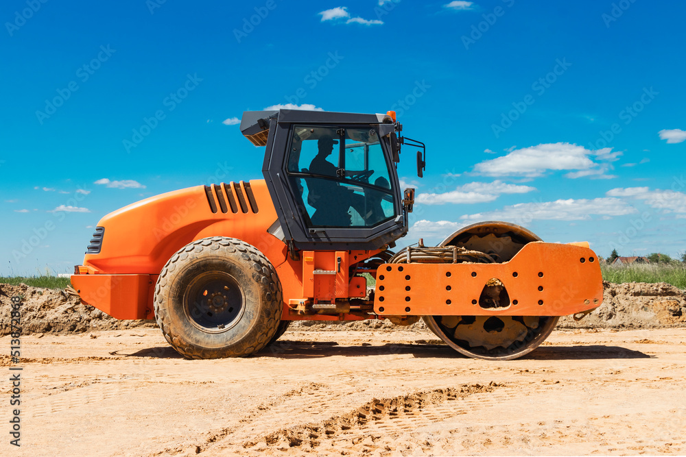 Powerful heavy road roller with a closed cabin against a blue cloudy sky. The skating rink prepares the ground for the construction of a new road. Road construction equipment. Powerful heavy road roller with a closed cabin against a blue cloudy sky. The skating rink prepares the ground for the construction of a new road. Road construction equipment.