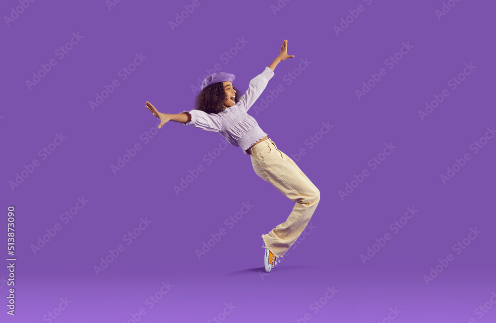 Cheerful joyful african american teenage girl having fun getting on her toes on purple background. Funny stylish preteen girl fooling around, rejoicing and laughing out loud. Full height. Banner.