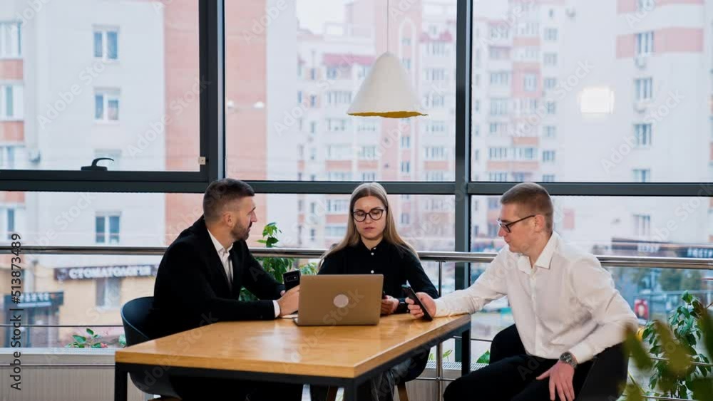 Office team having conversation sitting at the desk. Woman in the middle facing computer and men holding phones in their hands. Office team having conversation sitting at the desk. Woman in the middle facing computer and men holding phones in their hands.