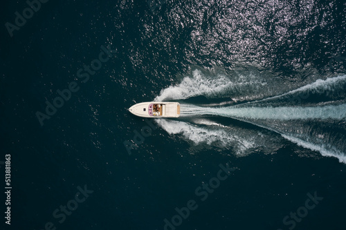 Big white speedboat moves fast on dark water top view. Big white boat with people moving on the water aerial view. © Berg