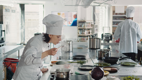 Woman working as cook testing bad soup for gourmet dish, making mistake in preparing culinary recipe. Authentic chef doing taste test with sauce, cooking in professional gastronomy kitchen. photo