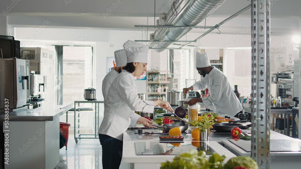 Female chef cooking gastronomy dish with vegetables on stove, making culinary recipe with bell pepper. Woman in uniform preparing food ingredients to cook delicious restaurant meal. Female chef cooking gastronomy dish with vegetables on stove, making culinary recipe with bell pepper. Woman in uniform preparing food ingredients to cook delicious restaurant meal.