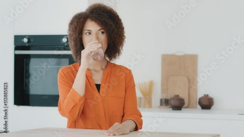 Thirsty African American woman with curly hair girl drinking water standing in kitchen in morning start new day with healthy habit holding glass drink clean mineral natural still beverage aqua balance