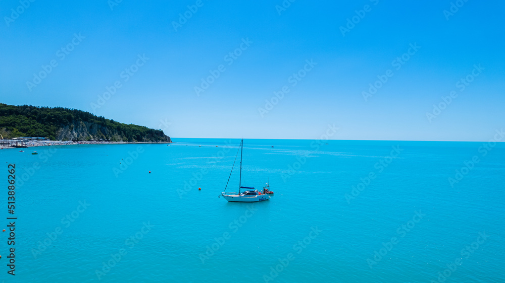 Amazing aerial view of Black Sea coast, turquoise color of the sea. Summer landscape with mountains, green forest, azure water, and blue sky in bright sunny day. Travel background. Top view.