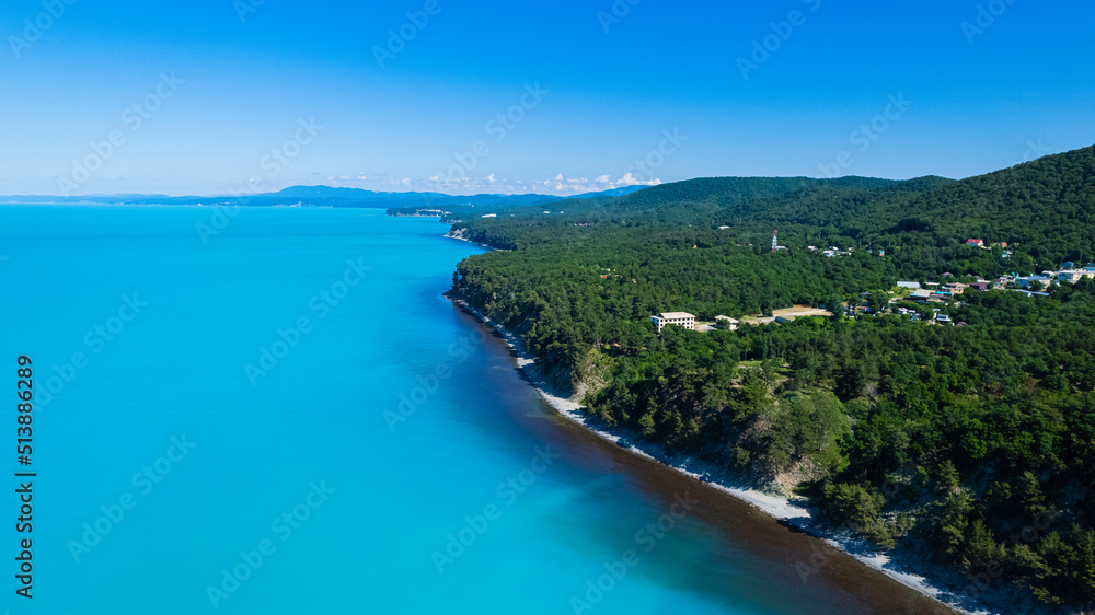 Amazing aerial view of Black Sea coast, turquoise color of the sea. Summer landscape with mountains, green forest, azure water, and blue sky in bright sunny day. Travel background. Top view.