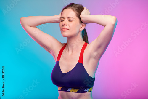 Woman with headache pain touching her head with eyes closed. Girl in sportswear. Female fitness portrait isolated on neon pink blue color background.