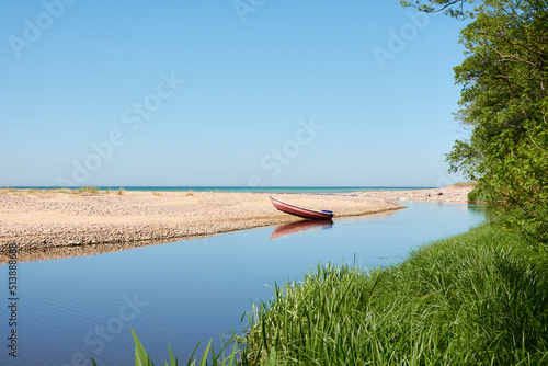 Small boat standing on the beach (sand dunes). River flowing into the Baltic sea. Clear blue sky, reflections on water. Nature, ecology, ecotourism, sport, wanderlust, boating, fishing, swimming theme photo