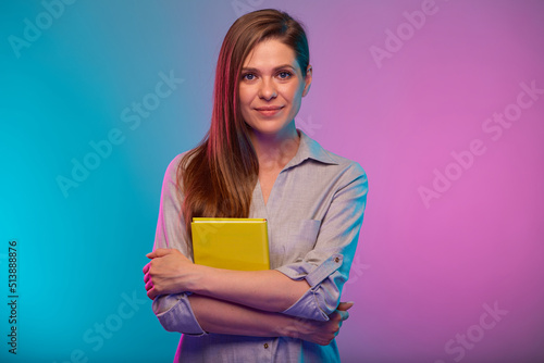 Confident teacher or student woman holding yellow book, portrait with neon lights colors effect. Female model isolated on neon background.