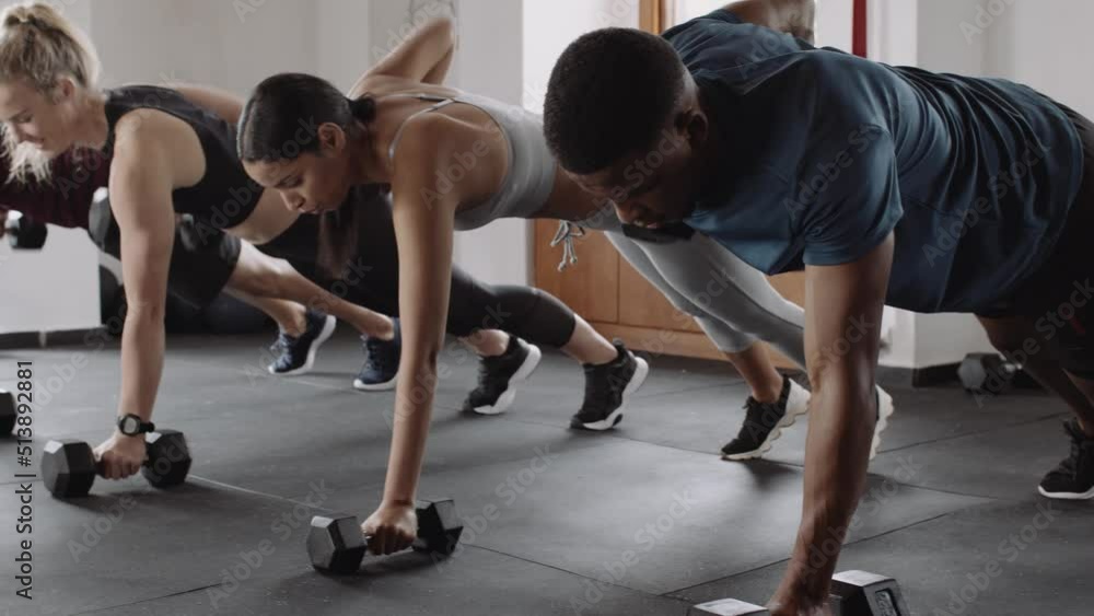 Group of diverse young adult friends exercising at an indoor fitness gym. Lifting weights in planking position. Group of diverse young adult friends exercising at an indoor fitness gym. Lifting weights in planking position.